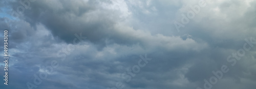 Dark storm clouds gather across the blue sky during the rainy season, forming dramatic shapes as nature signals an approaching storm over the open landscape.