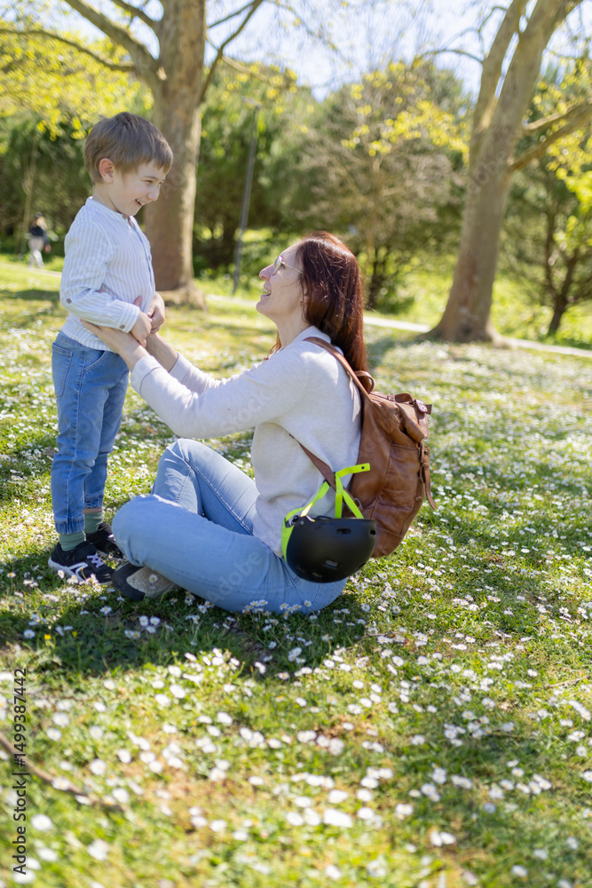 Fototapeta premium Mother kneeling on grass holding her son's hands in park