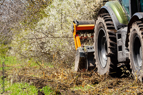 Against a background of nature, a tractor-type machine is captured cutting and clearing forests in nature. Deforestation is a big problem. This device cuts everything in its path such as trees, bushes