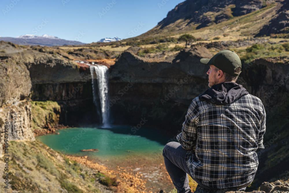 Man tourist gazing at the Salto del Agrio waterfall plunging into a turquoise pool. Neuquen, Argentina Man tourist gazing at the Salto del Agrio waterfall plunging into a turquoise pool. Neuquen, Argentina