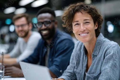 A cheerful group of diverse professionals collaborate in a bright and modern workspace, embodying positivity and teamwork while utilizing digital devices during a productive session.