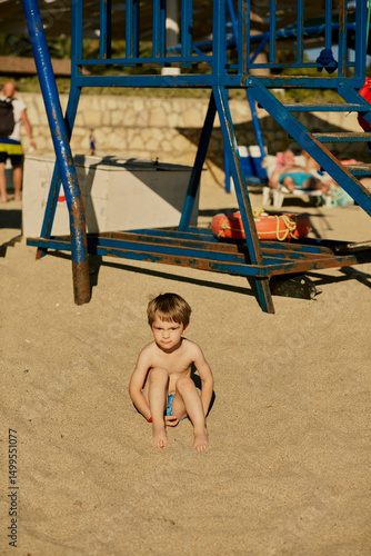 Little 3 year old boy is playing on the beach under the sun.