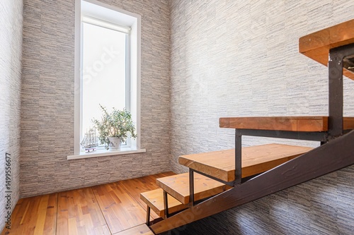 interior shot features wooden stairs with metal supports next to a window. A plant sits on the windowsill.