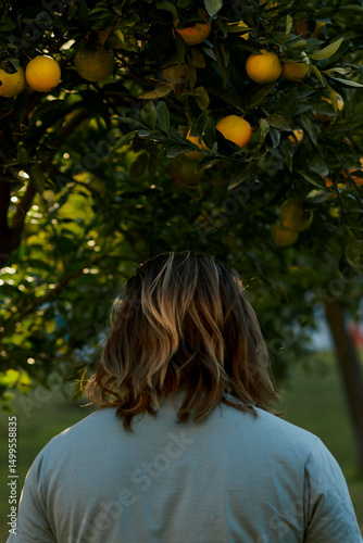 Long-haired man standing back to camera under the orange tree in Turkey.