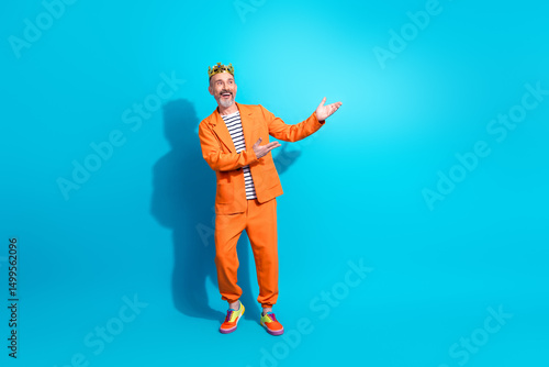 Canvas Print Stylish adult man in vibrant orange suit and crown showing gesture on cheerful b