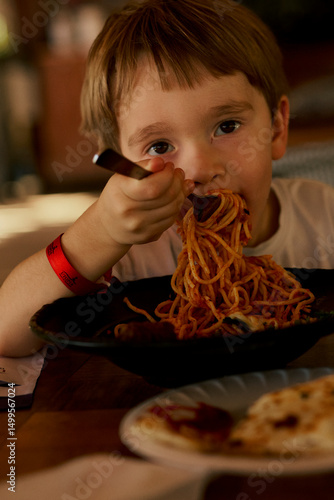 Little boy eating a spaghetti with tomato sauce.
