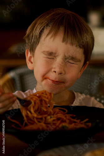 Little boy eating a spaghetti with tomato sauce.
