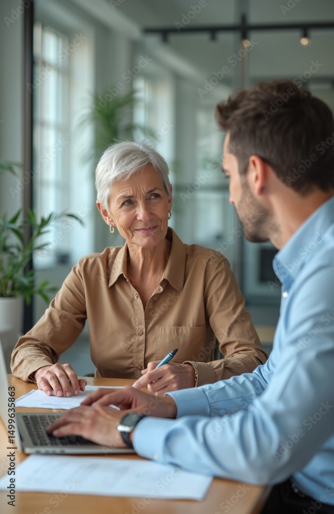 Obraz premium Middle-aged businesswoman, male colleague collaborate in office, discussing project. Teamwork, advisory session, financial meeting at workplace. Executive manager, employee partnership. Office