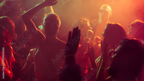 Obraz na plátne Vibrant party scene with diverse individuals dancing in a dimly lit, smoke-filled club with vibrant red and orange lighting