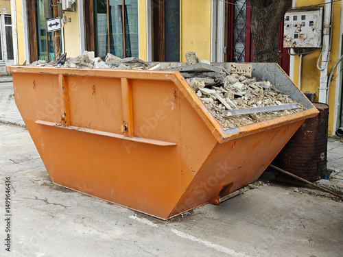 Orange Industrial Dumpster Full of Construction Debris and Rubble on Urban Street. Building Renovation Waste Management and Cleanup Concept