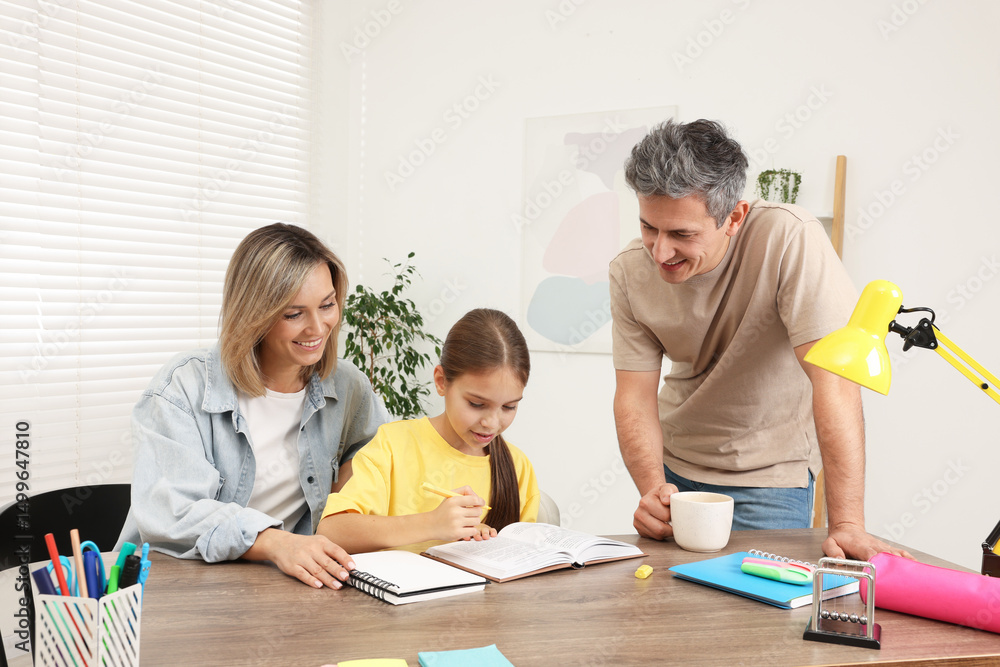 Smiling parents helping their daughter with homework at table indoors Smiling parents helping their daughter with homework at table indoors