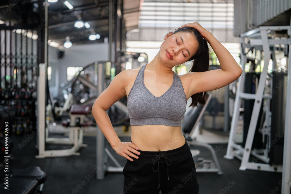 Fototapeta premium Fit young woman in sportswear stretching neck muscles before workout in a gym.
