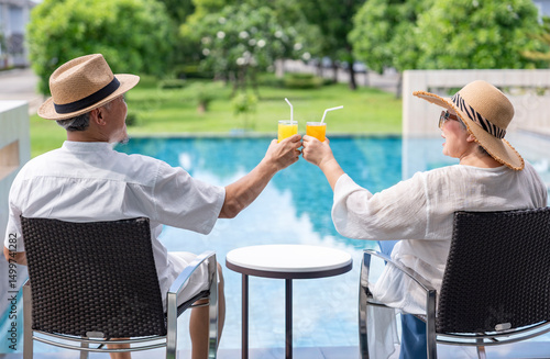 happy senior couple enjoy talking with freshy drink on table,sitting,relaxing by the pool,elderly people travel destination tropical resort and spa on summertime