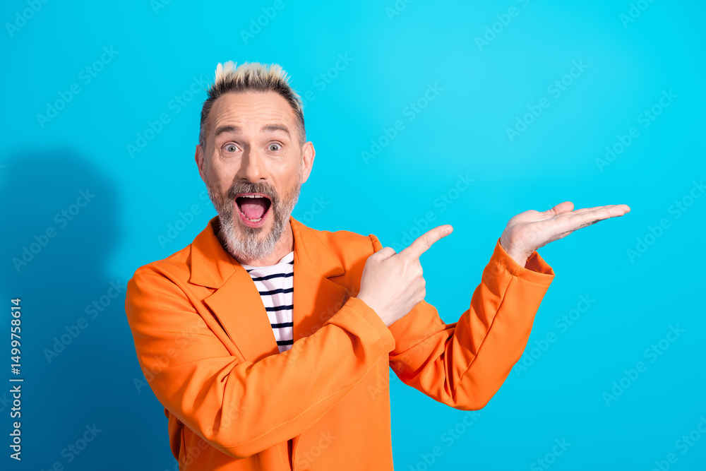 Naklejka premium Vibrant mature man in orange jacket presenting on a blue background with expressive gestures and joyful expression