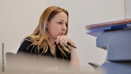Thoughtful woman stares at screen in silence while mumbling in office setting