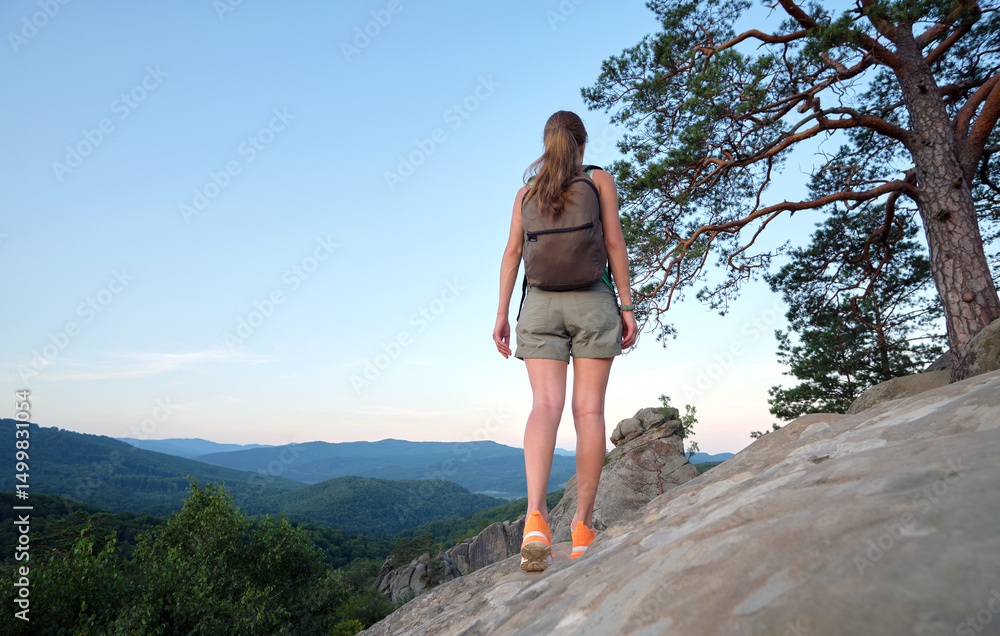 Naklejka premium Hiker woman walking on mountain footpath enjoying evening nature. Lonely female traveler traversing wilderness trail. Healthy lifestyle concept