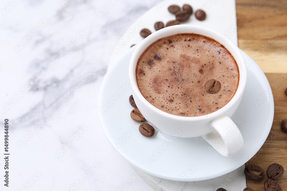 Obraz premium Aromatic coffee in cup, beans and saucer on white marble table, closeup. Space for text