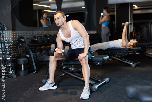 Wallpaper Mural Young man in gym lifts dumb bell, participates in workout to strengthen muscles of his arms. Male sportsman works independently with weight, works out slimness and attractive figure Torontodigital.ca