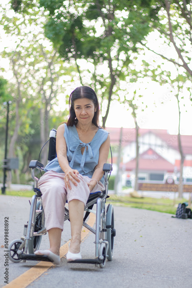 Obraz premium A smiling elderly woman in a wheelchair sits outdoors with her caregiver, sharing a hopeful conversation during a rehabilitation treatment for arthritis in her leg.