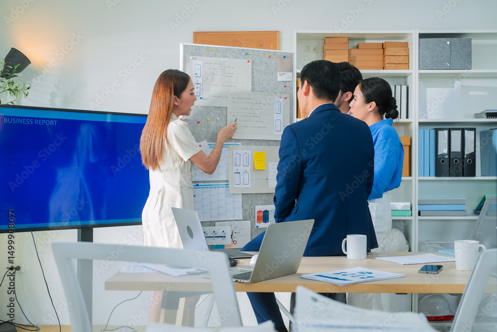 Obraz premium Business team stands around a flip chart, brainstorming app structure and workflow, sharing ideas, mapping flowcharts, and creating an inclusive, hands-on experience in a collaborative meeting