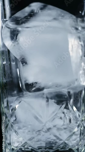 Pouring Clear Liquid Over Ice Cubes in Crystal Glass Close Up
