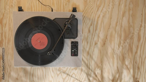 Overhead shot of a modern vinyl record player with a spinning black record, placed on a light wood background, representing retro music. Copy space, wooden surface, table