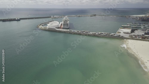 Drone flies sideways over port on calm Atlantic Ocean with a cruise ship docked on a sunny afternoon