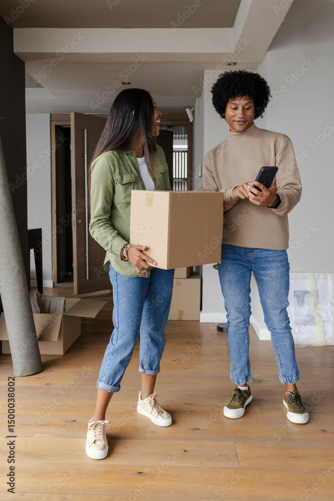 Unpacking Diverse couple organizing moving boxes in empty room, with smartphone and rolled-up rug Unpacking Diverse couple organizing moving boxes in empty room, with smartphone and rolled-up rug