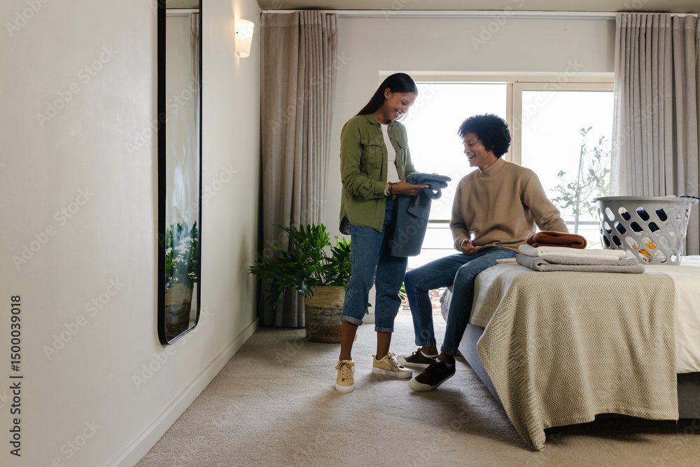 Diverse couple folding clothes in modern bedroom, with laundry basket and plant, copy space Diverse couple folding clothes in modern bedroom, with laundry basket and plant, copy space