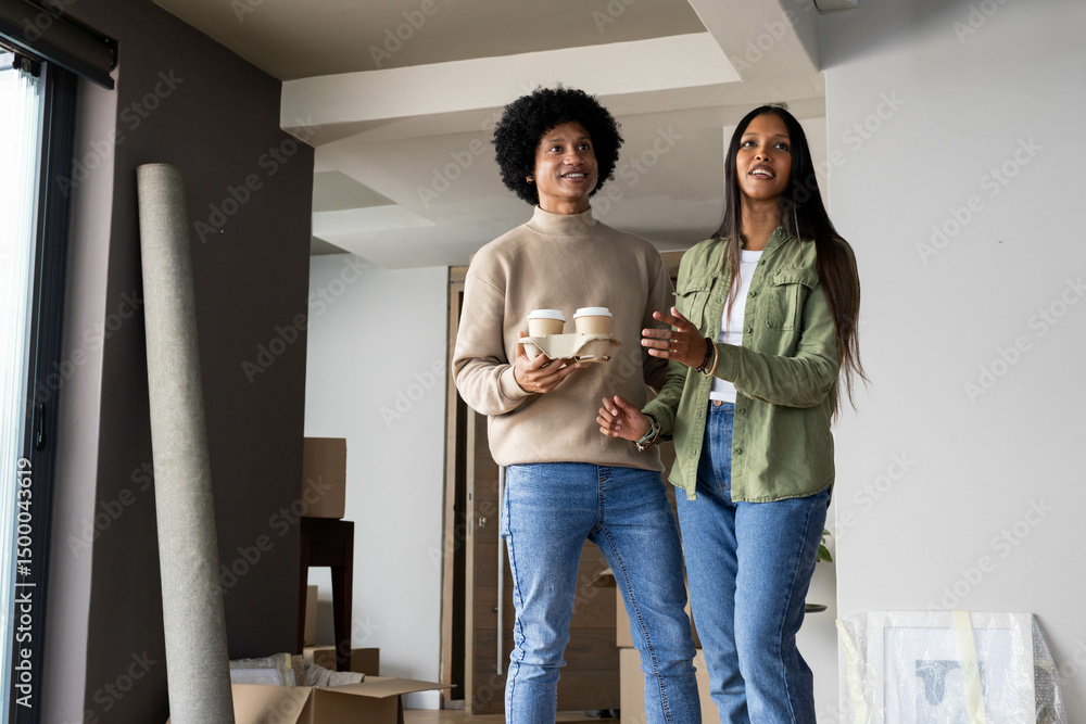 Standing Diverse couple inspecting bare room with coffee cups, moving boxes and rolled-up carpet Standing Diverse couple inspecting bare room with coffee cups, moving boxes and rolled-up carpet