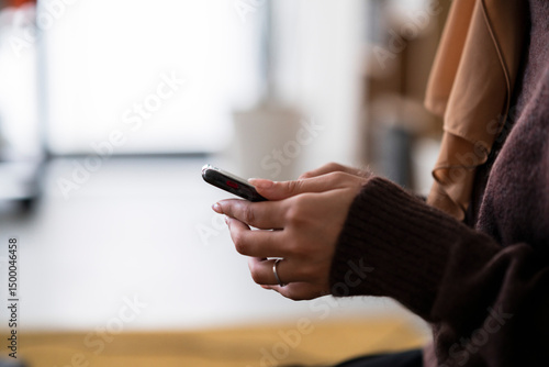 A person is holding a smartphone, their fingers interacting with the screen. They are using the device to connect with others or access information, staying connected.