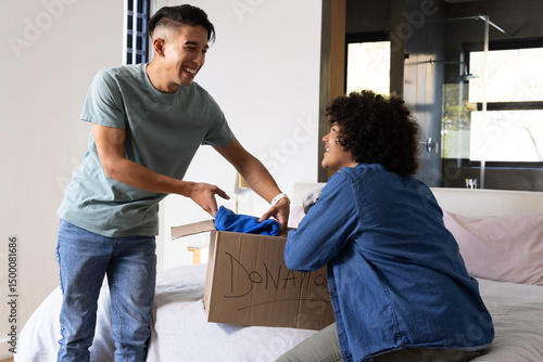 Organizing Diverse male friends sorting clothing in bedroom with Donation box and shirt, copy space