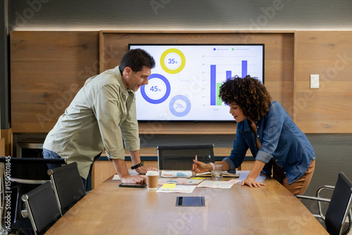 Reviewing Diverse coworkers leaning over conference table in conference room, with printed charts