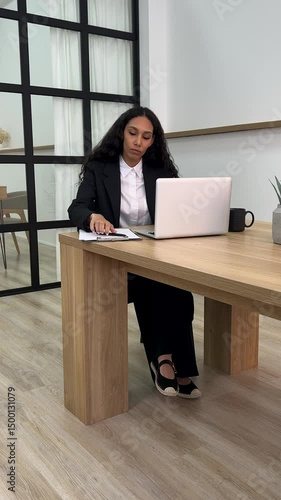 A European girl is talking on a cell phone, smiling sweetly, making notes on a piece of paper, a diary. Finishes the conversation and continues working on the computer