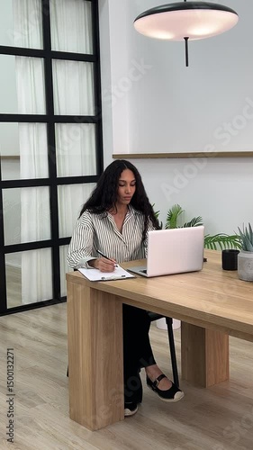 African American university student studies with laptop making notes on paper modern technology education. Mid adult black student using laptop and takes notes paper while studying university.