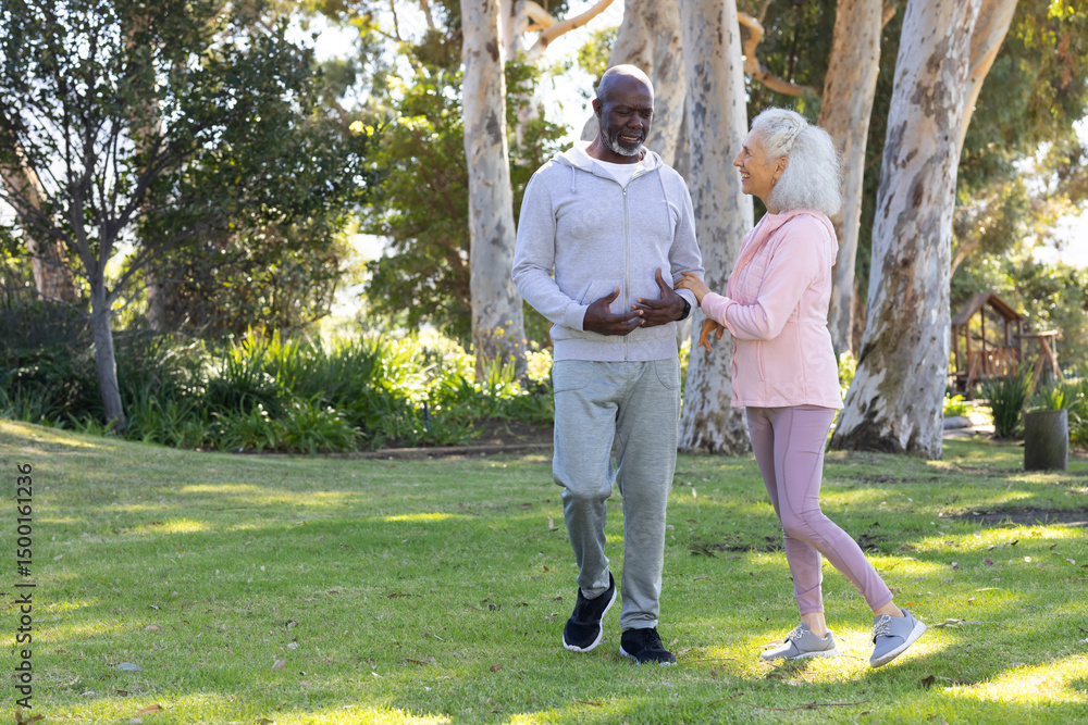Walking diverse couple chatting on grassy lawn in park, with dappled sunlight through trees Walking diverse couple chatting on grassy lawn in park, with dappled sunlight through trees