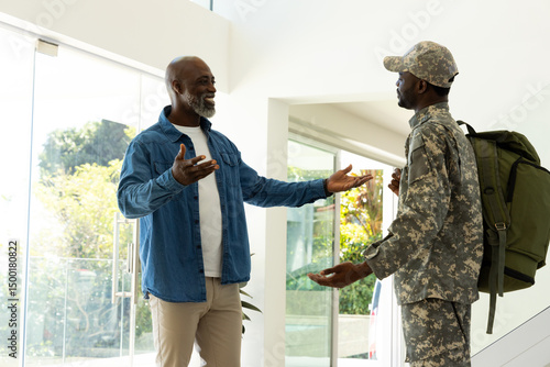 Greeting African American father and son hugging in entryway, with camouflage uniform and backpack