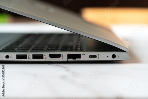 Close up detail of the side panel connectivity on a modern laptop, showing various input and output ports including USB, USB-C, HDMI, and audio jack for peripheral connection on an office desk.