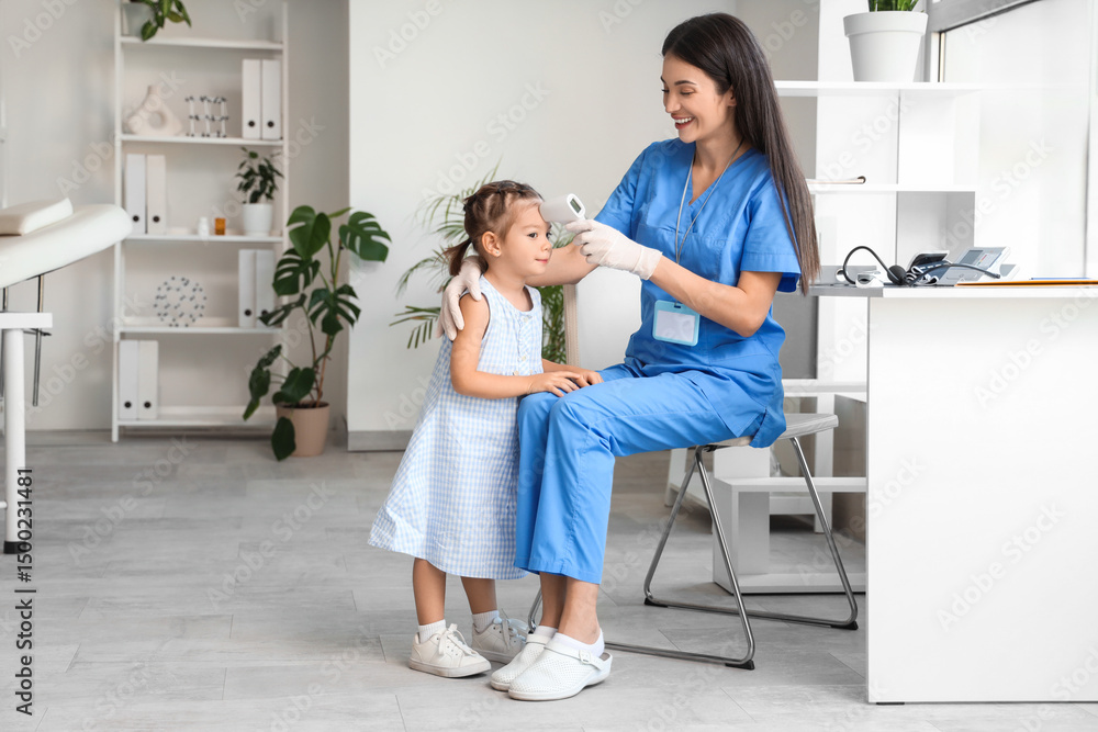 Fototapeta premium Female pediatrician with infrared thermometer measuring little girl's temperature in clinic
