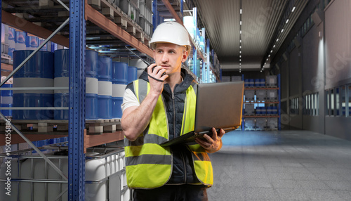 Photos Warehouse supervisor with laptop and walkie-talkie checks inventory of chemical barrels on industrial shelving