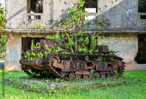 Rusted Japanese tank from World War II, now overtaken by tropical plants, sits abandoned in front of the bomb-damaged Japanese Communications Center in Palau. The fusion of corroded steel and vibrant