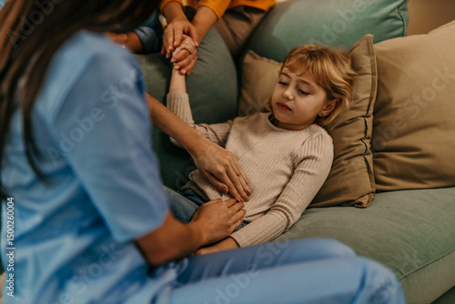 Tableau sur toile Pediatrician examining little girl's abdomen at home: doctor performing palpatio