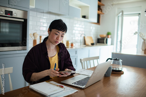 фотографія Stressed woman reviewing bills and finances on laptop at kitchen table