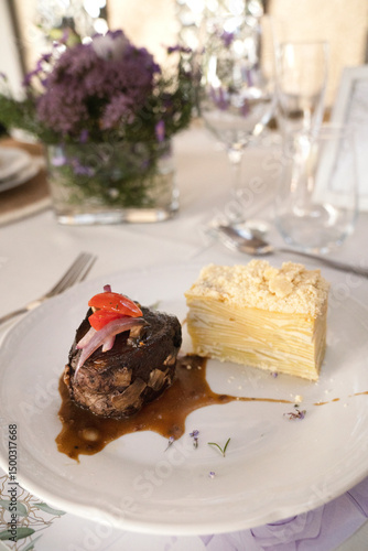 Gourmet gastronomy in a social event. Closeup view of a grilled loin fillet with sauce and a potato mille feuille in a white dish on the gala table