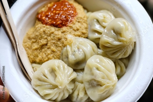 A paper plate of assorted momos served with spicy chutney and wooden fork and knife at a Nepalese street food stall in Little India - Harris Park, Sydney, New South Wales, Australia 