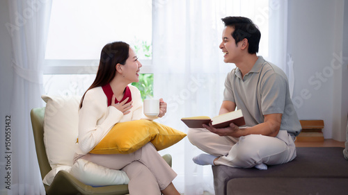 Asian Couple Relaxing at Home with Book and Coffee Sharing Joyful Moments Together in Cozy Living Room Promoting Bonding