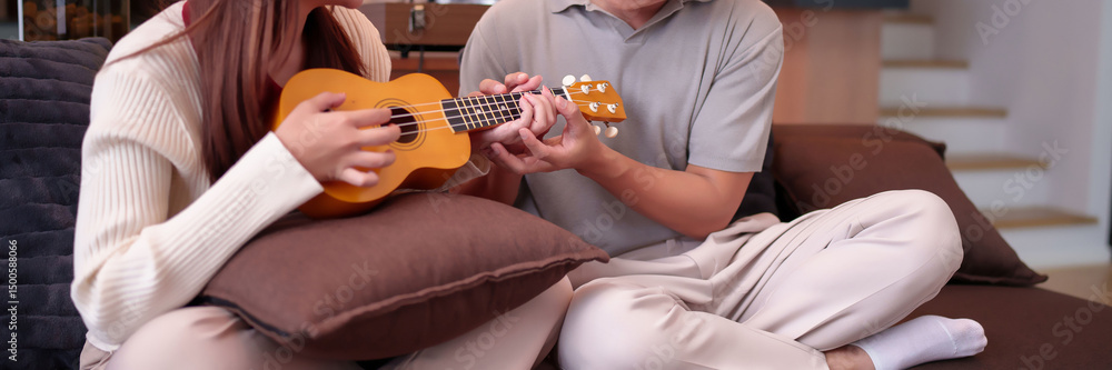 Fototapeta premium Asian Couple Play Ukulele Together Relaxing on Sofa at Home Leisure Time with Musical Instrument and Harmony Relationship for Adult