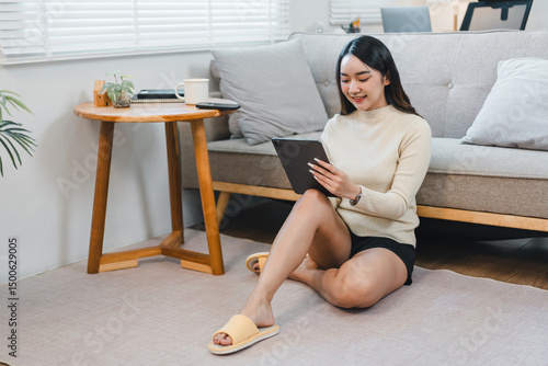 Free Download Young Asian woman sitting on floor in living room, smiling while using digital tablet, casual home environment, relaxed and comfortable atmosphere, modern interior design - GFXLoad