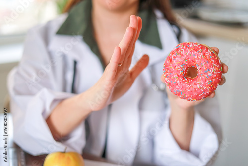 Nutritionist shows a sugary donut as an example of an unhealthy choice and its impact on health. Health and nutrition concept.