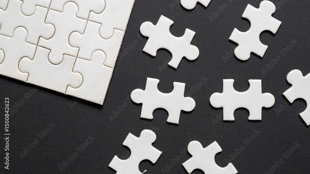 Fototapeta premium “Scattered white jigsaw puzzle pieces on black leather textured background. Concept image representing problem solving, decision making, strategic planning, missing piece, teamwork, or confusion.”